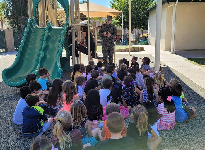 A photo of children listening to a military officer speak to them