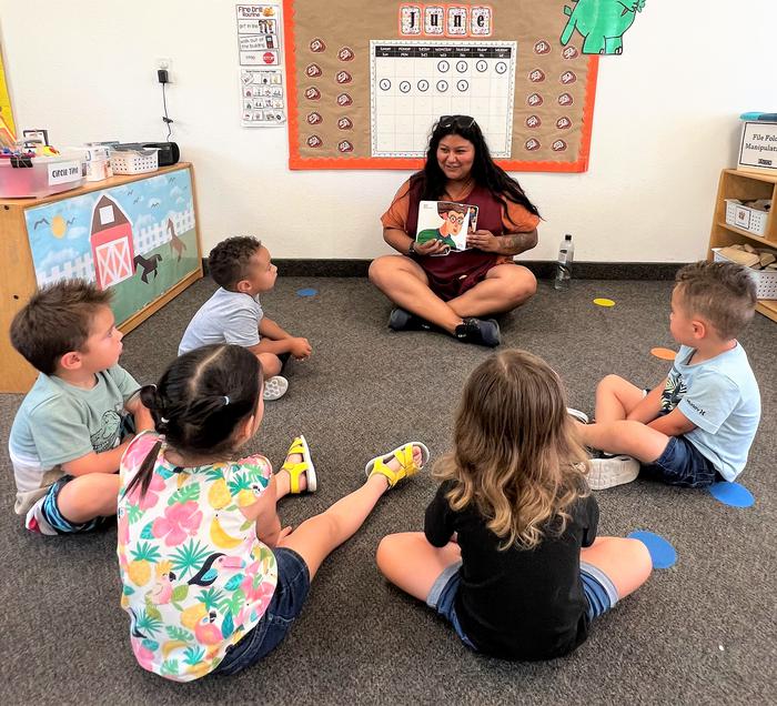 A group of children reading a book with their teacher. 