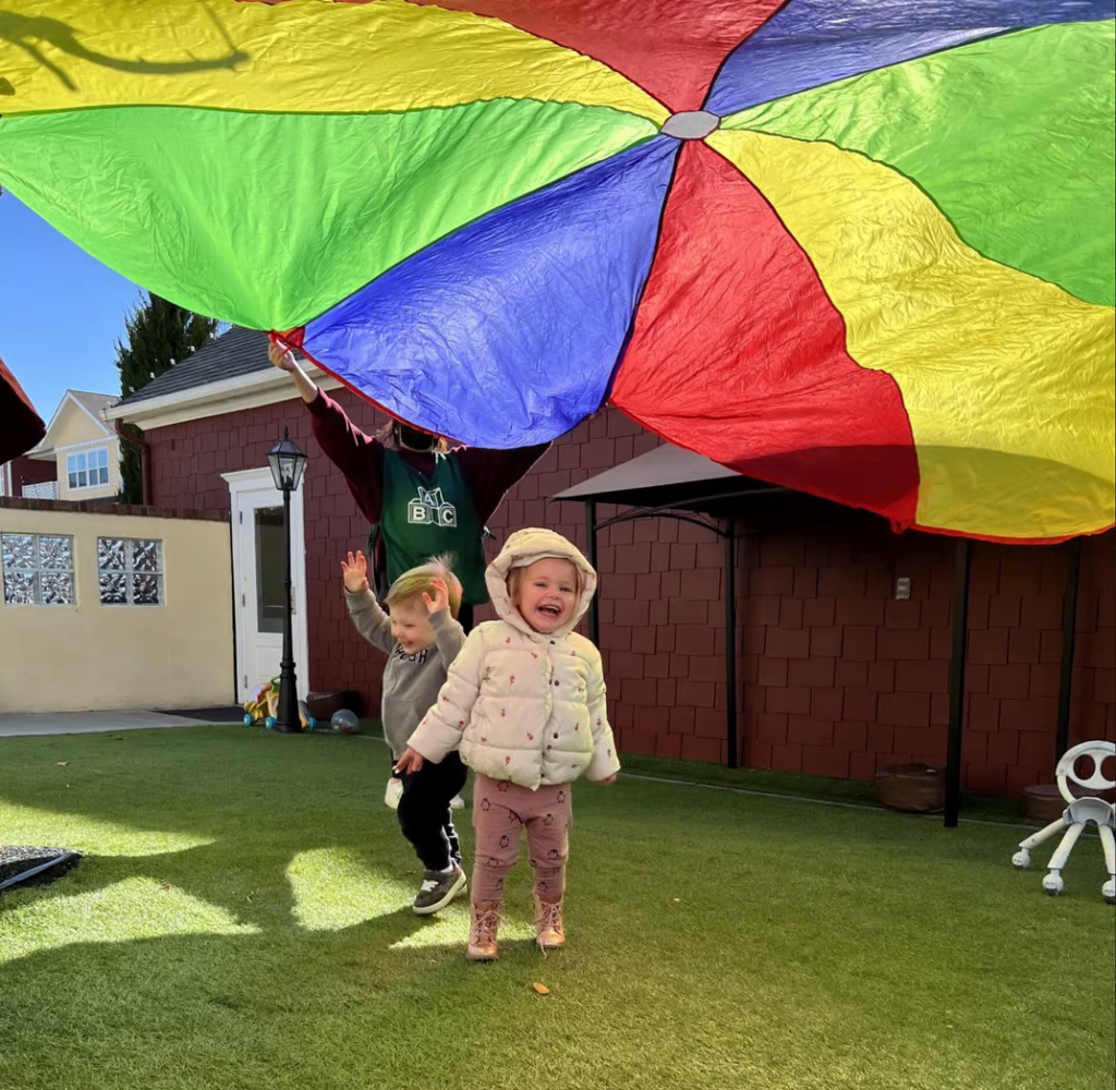 Child underneath a rainbow colored parachute