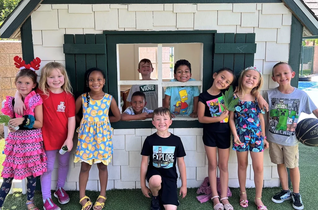 A group of children standing in front of a house and smiling.